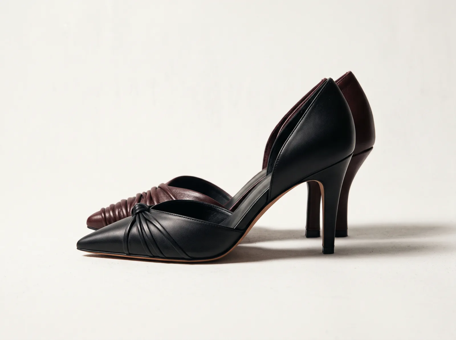 A black and an oxblood Channah heel side by side on a warm white studio ground