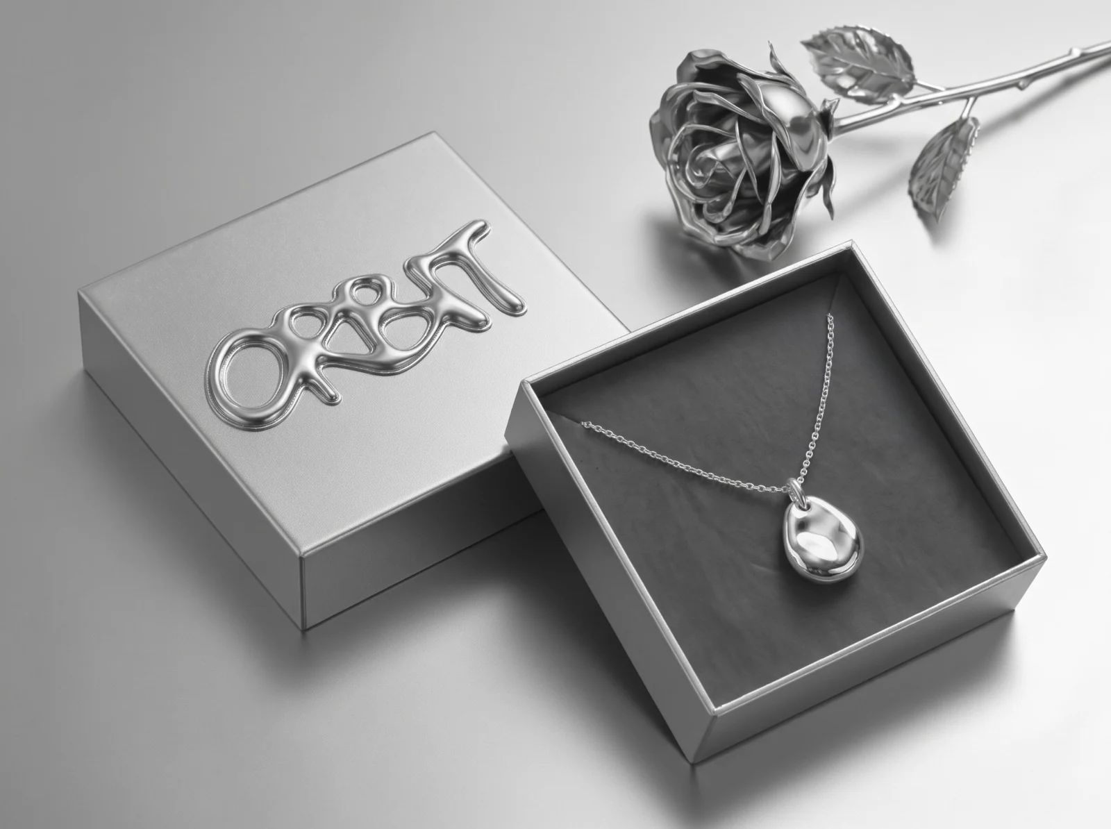 ORBIT box with the chrome wordmark raised on its lid, a silver pebble pendant in the open box and a silver rose beside it
