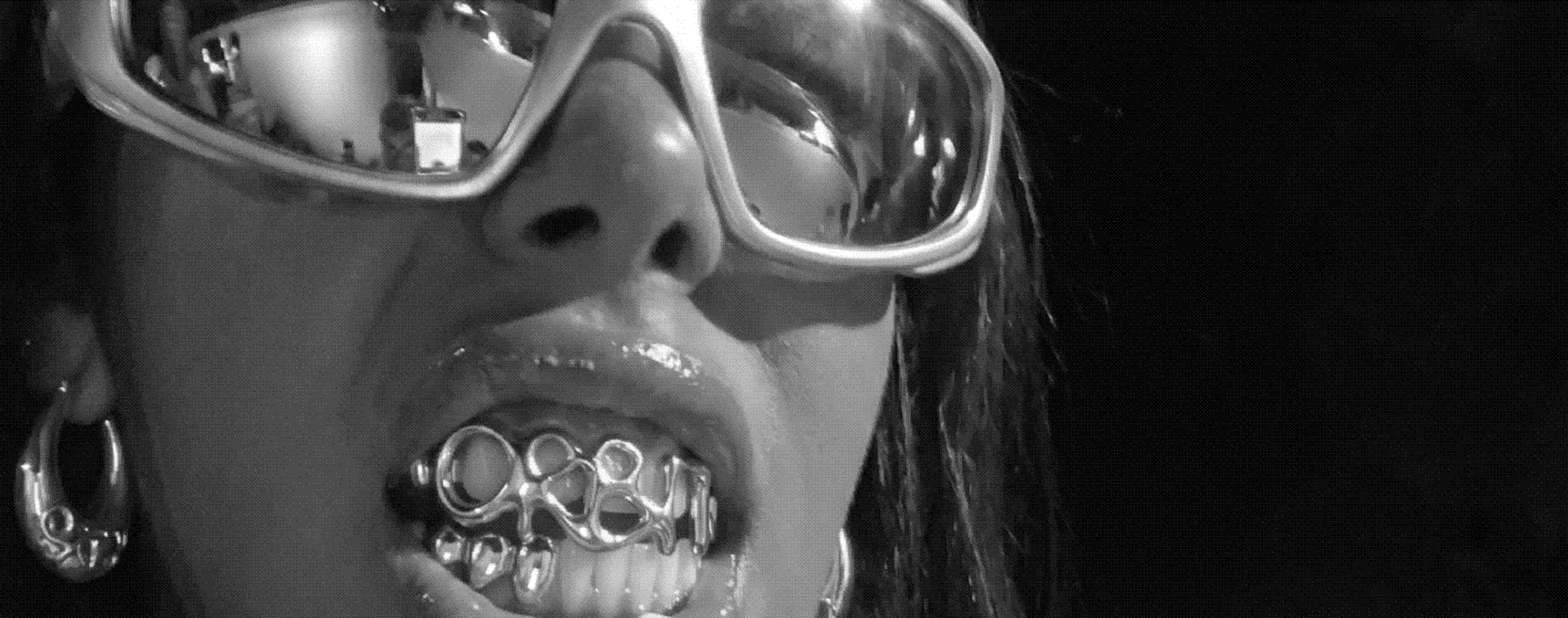 A woman in chrome sunglasses showing ORBIT grillz and a silver hoop