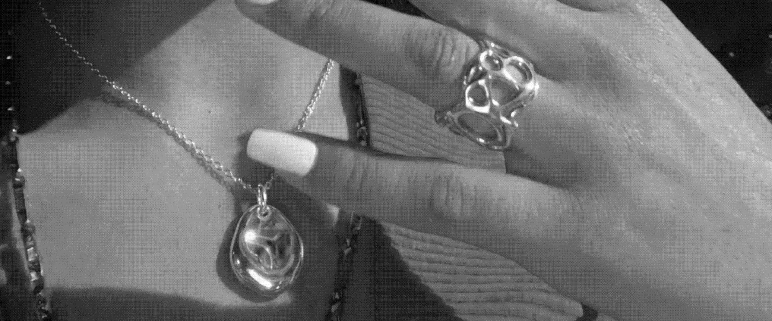 A hand wearing the Flux ring over the Orbit pendant